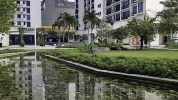 A modern urban setting with high-rise buildings, a calm water feature with rocks, and well-maintained greenery.