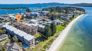 Vue aérienne d’un quartier résidentiel situé sur la côte, avec une plage, une marina et un hôtel imposant, doté de plusieurs étages et de balcons.