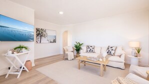 Un salon moderne avec un canapé blanc, une table basse et un grand téléviseur à écran plat qui diffuse une scène de plage.
