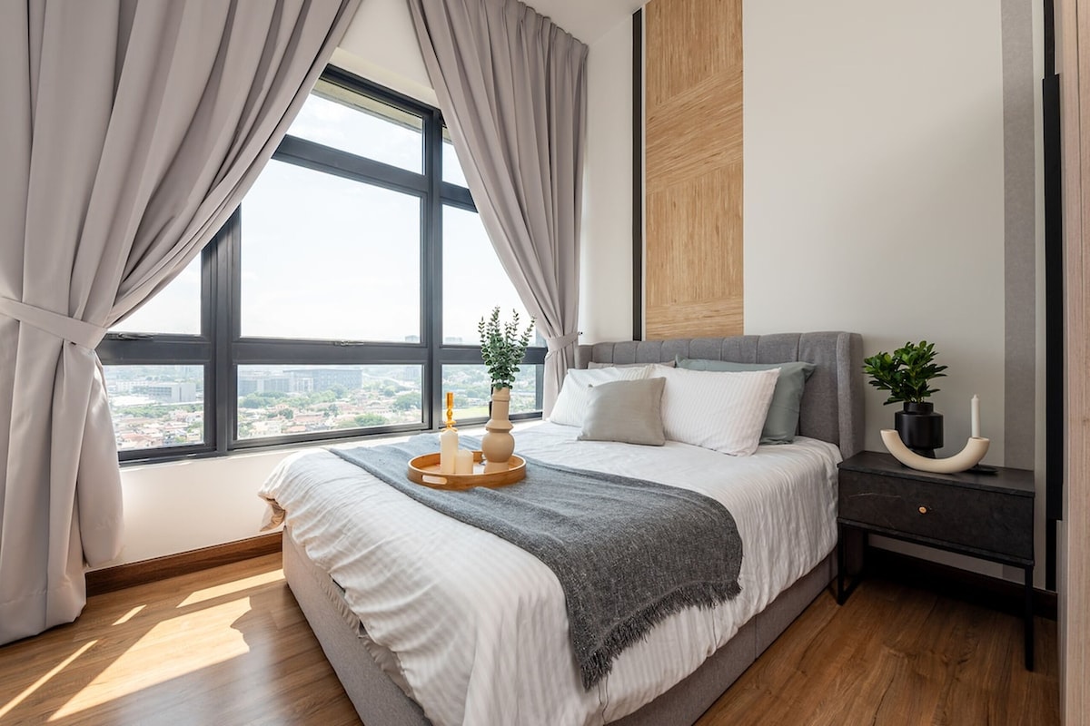 Een moderne slaapkamer met een groot bed, een nachtkastje met een plantje en uitzicht op de stad door een groot raam.