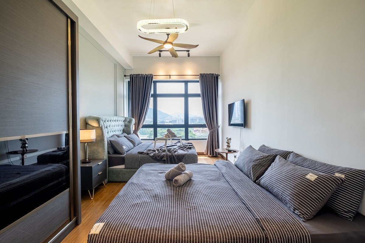 Een moderne hotelkamer met een groot bed, een slaapbank, een bureau en uitzicht op de stad door grote ramen.