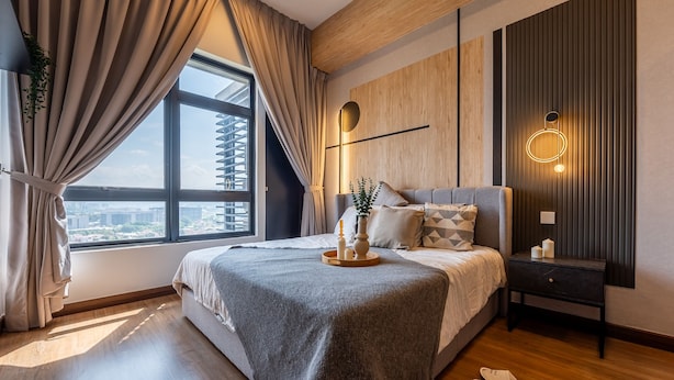 Une chambre moderne avec un grand lit, une table de chevet, une lampe fixée au mur et une vue sur la ville par la fenêtre.
