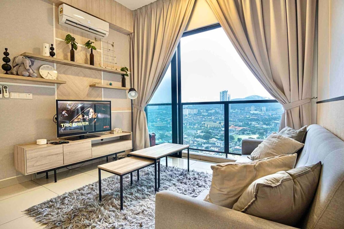 Een moderne woonkamer met een grote televisie, een bank, een salontafel en uitzicht op een stadsgezicht door grote ramen.