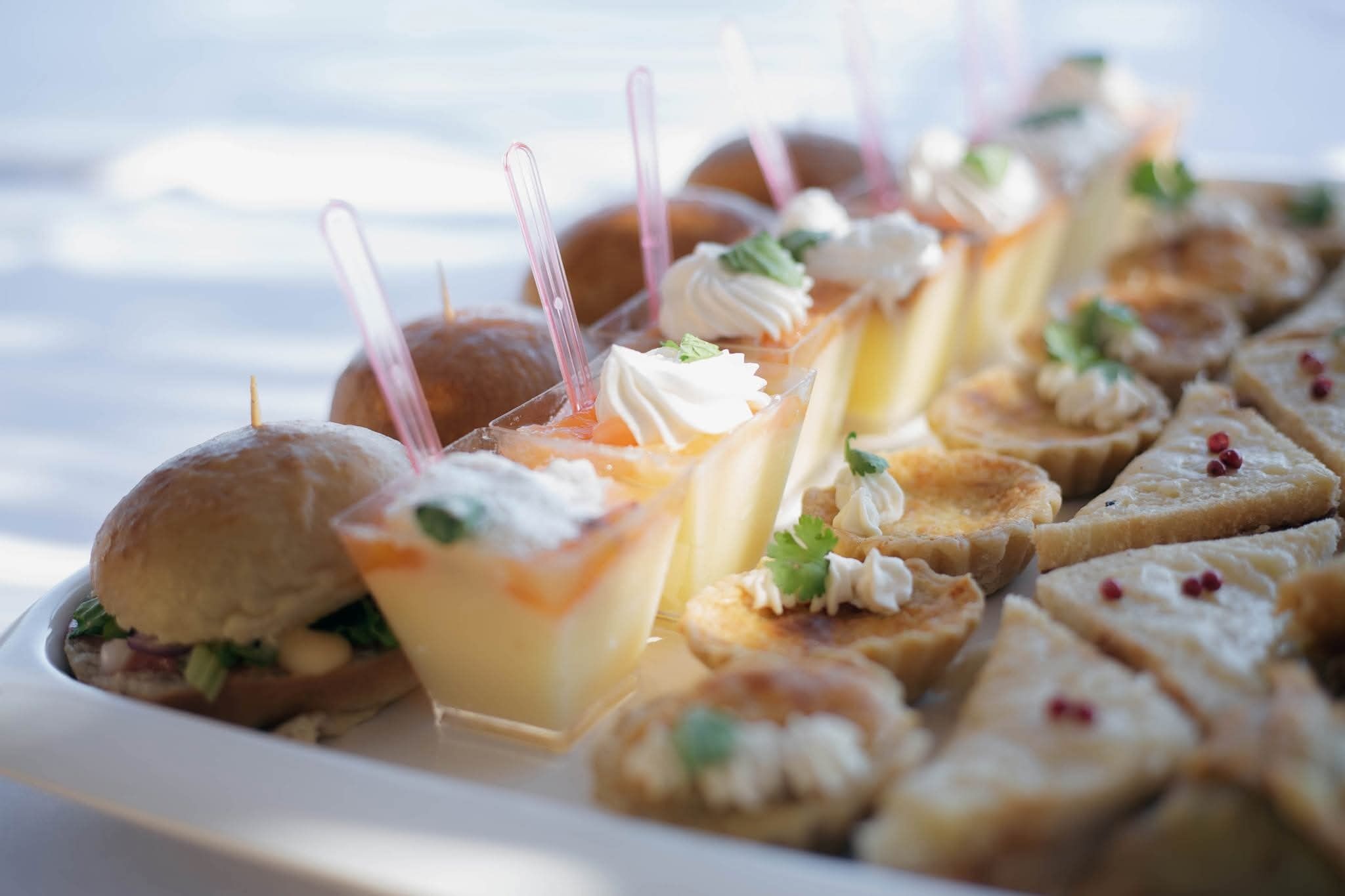 Una variedad de aperitivos, incluyendo mini sándwiches, un postre con crema batida y pequeñas pastas en un plato.