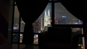 Habitación con un amplio ventanal que ofrece vistas a un paisaje urbano nocturno, con rascacielos iluminados y vistas de la ciudad.