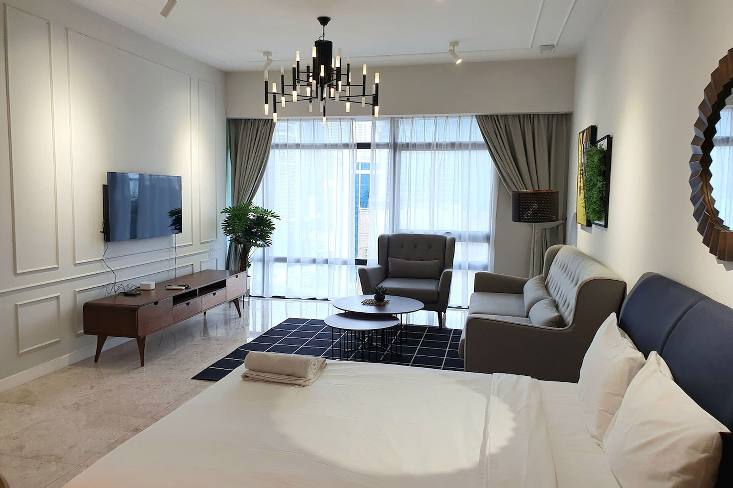 Una habitación de hotel moderna con una cama grande, un sofá, una silla, una mesita, un televisor y una planta en maceta.