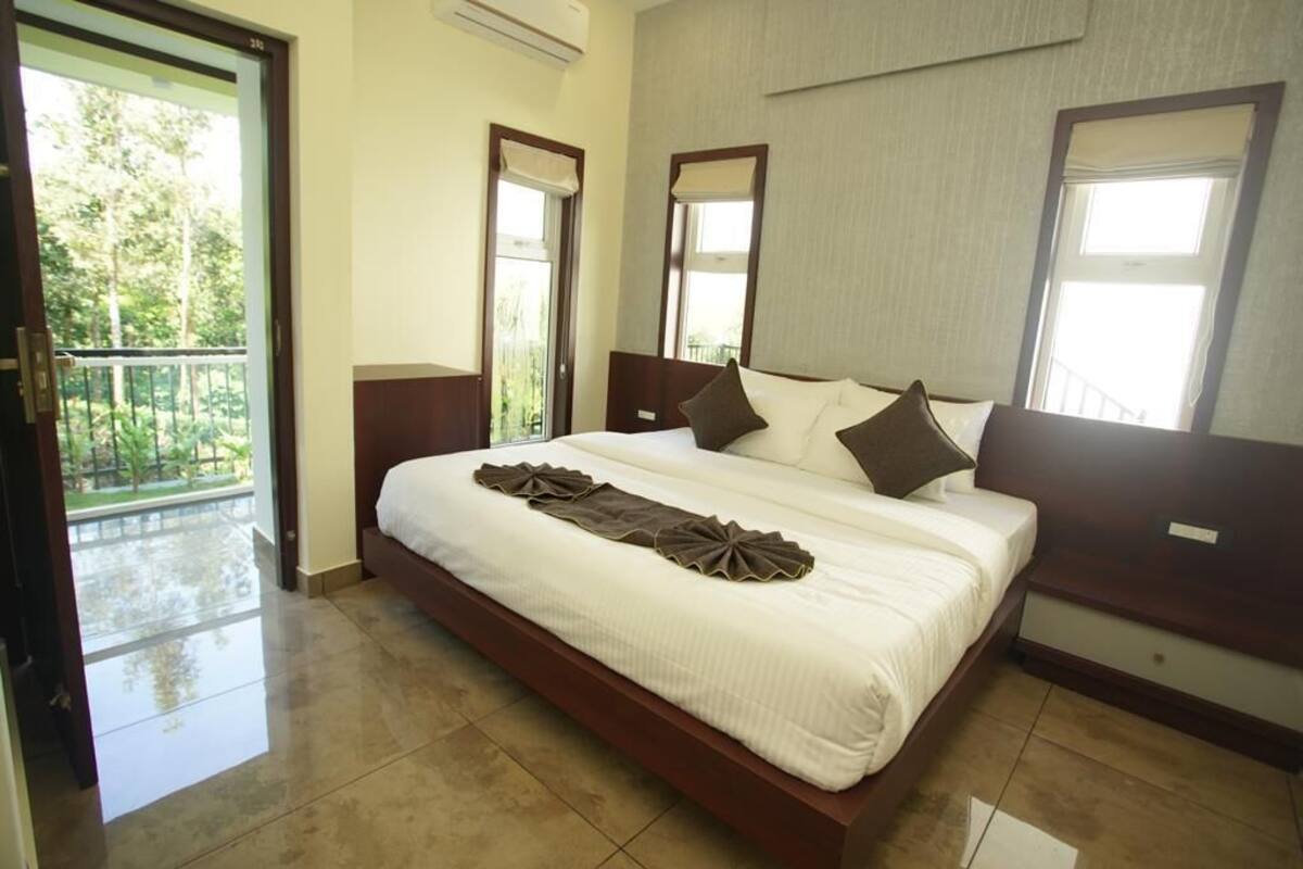 A spacious bedroom with a large bed, a balcony door, and a view of greenery outside.
