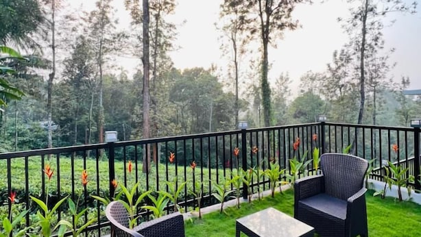 Eine Terrasse mit zwei Korbstühlen und einem Tisch, umgeben von einem schwarzen Geländer und üppigem Grün.