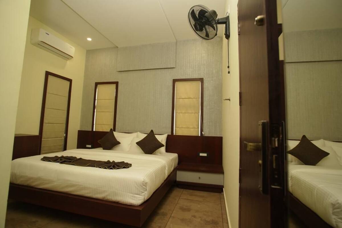 A hotel room with a large bed, bedside tables, a standing fan, and a door leading to another room.