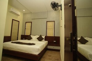 Ein Hotelzimmer mit einem großen Bett, Nachttischen, einem Standventilator und einer Tür zu einem weiteren Raum.