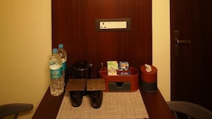 Ein Hotelzimmer mit einer Holztür, einem kleinen Tisch mit Unterlage, einer Wasserflasche, einer Papiertüte und einem Mülleimer.
