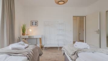 Quarto com duas camas, uma escrivaninha, uma cadeira, luminária pendente e um guarda-roupa.