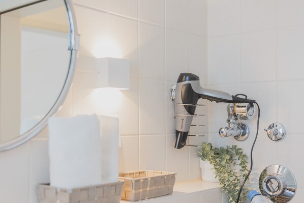 A bathroom with a hairdryer mounted on the wall, a mirror, a basket, and a potted plant.