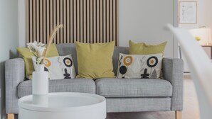 A grey sofa with patterned cushions, a white vase with flowers, and a wooden slat wall. - Rentaflat Norderstedt 2BR Apartment for 4 Guests (Norderstedt)