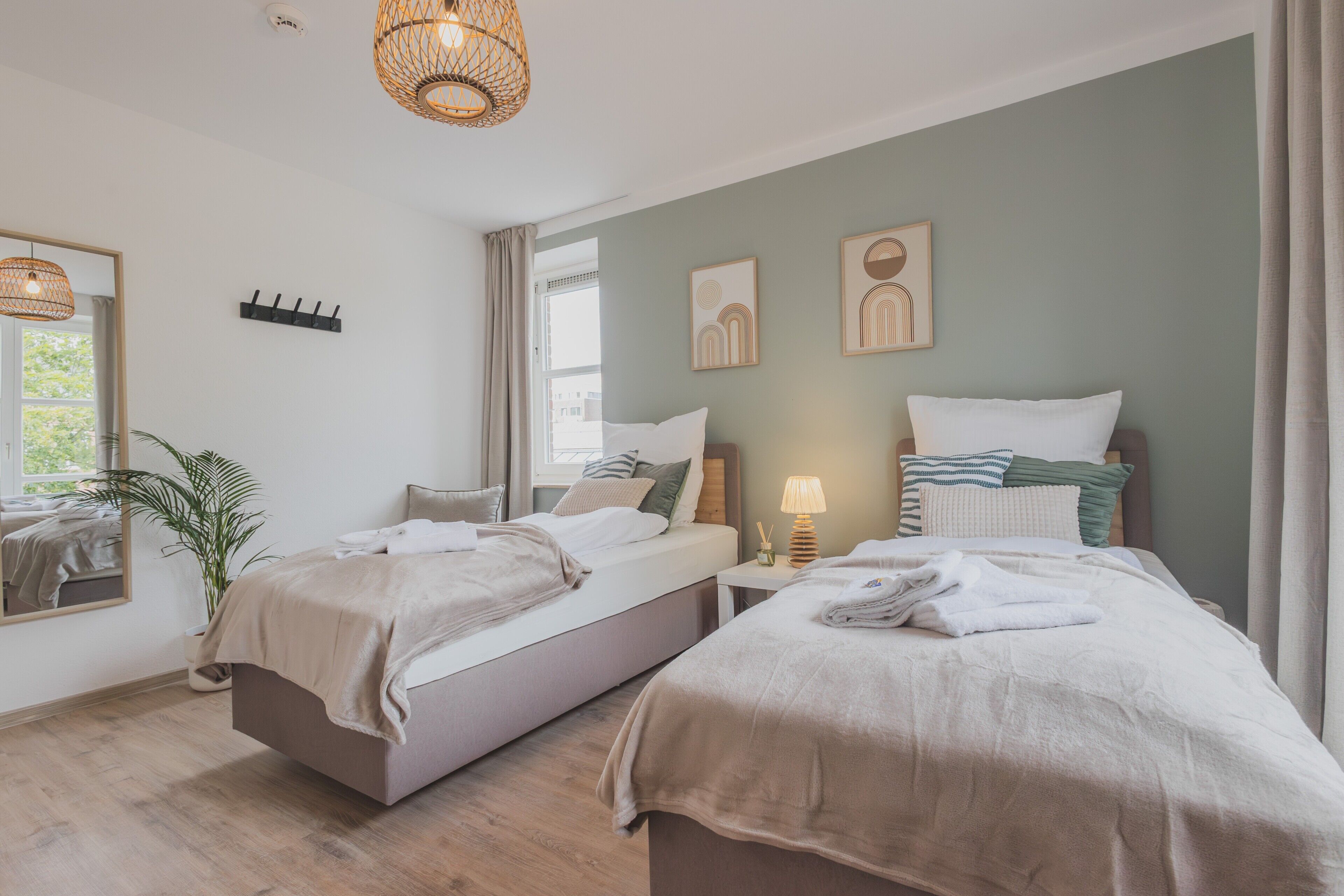 A bedroom with two beds, a bedside table with a lamp, a plant, and artwork on the wall.