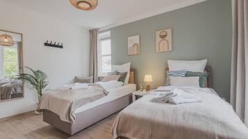 A bedroom with two beds, a bedside table with a lamp, a plant, and artwork on the wall.