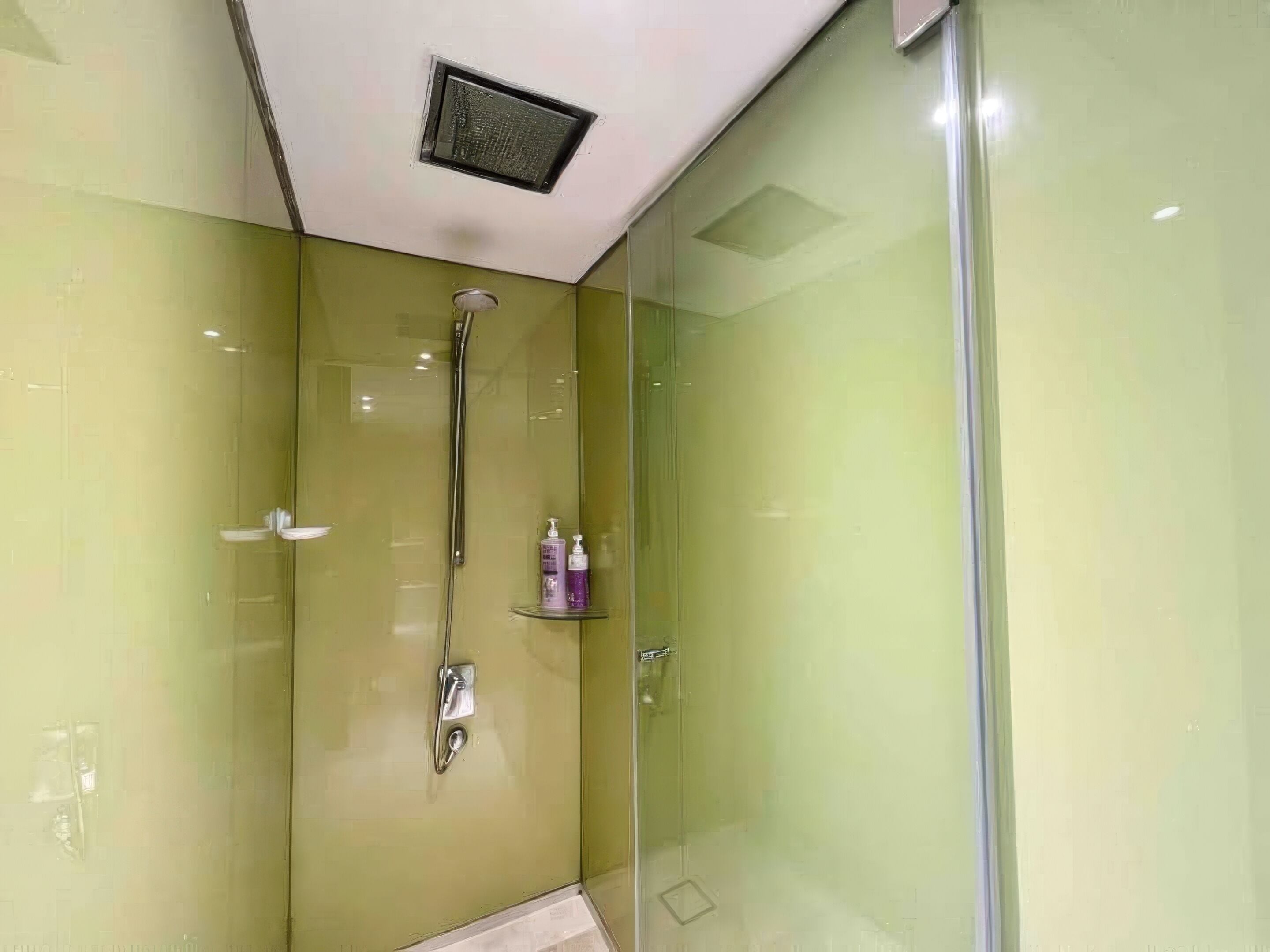 A modern bathroom with a glass shower enclosure, a handheld showerhead, and a small shelf with toiletries.