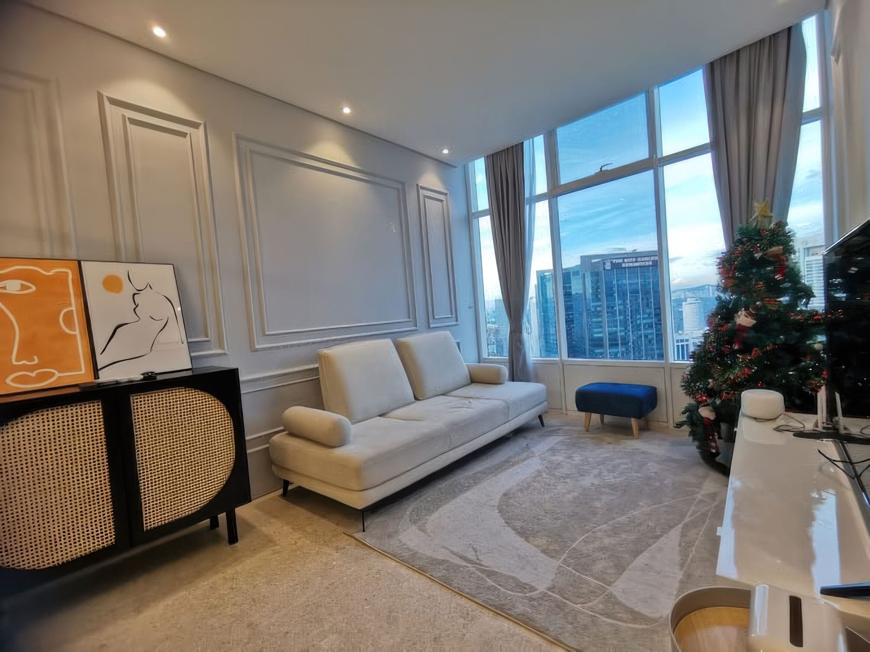 Una sala moderna con un sofá, un pequeño otoman, un aparador decorativo y un árbol de Navidad.