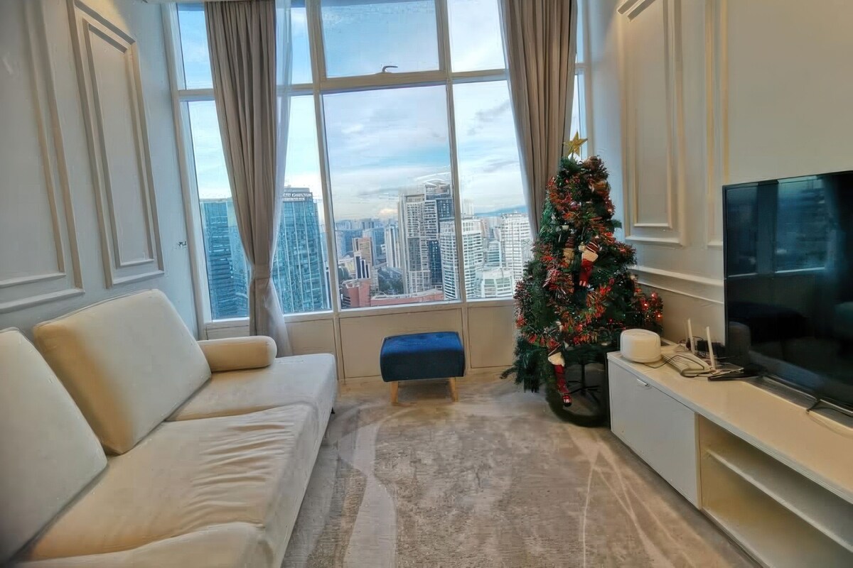 A modern living room with a large window, a sofa, a Christmas tree, and a flat-screen TV.