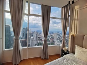 A bedroom with a large window, a bed, and a nightstand with a lamp.