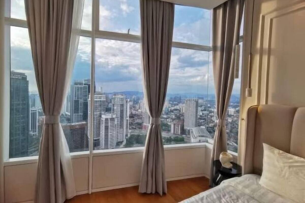 A hotel room with a large window, curtains, a bed, and a nightstand.