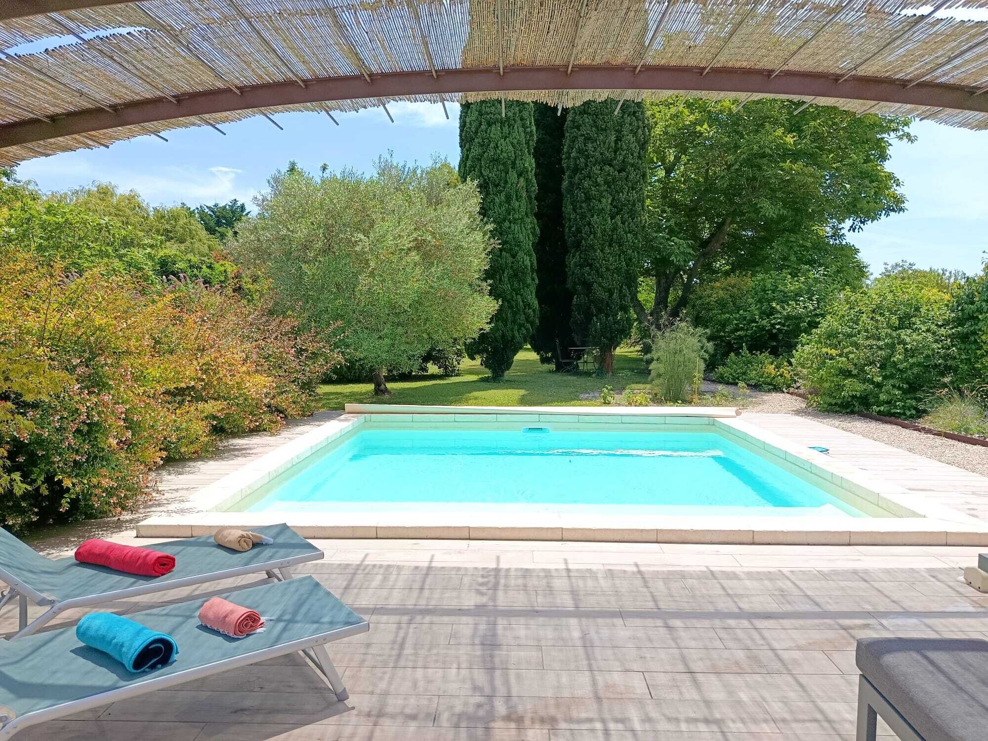 Ein Schwimmbecken mit Liegestühlen und einer Pergola darüber.