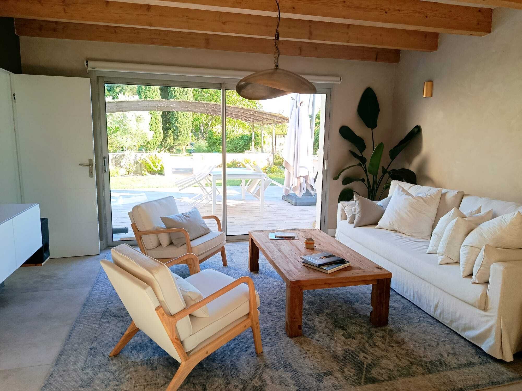 Un salon comprenant un canapé, deux fauteuils, une table basse et une grande fenêtre donnant sur un jardin.