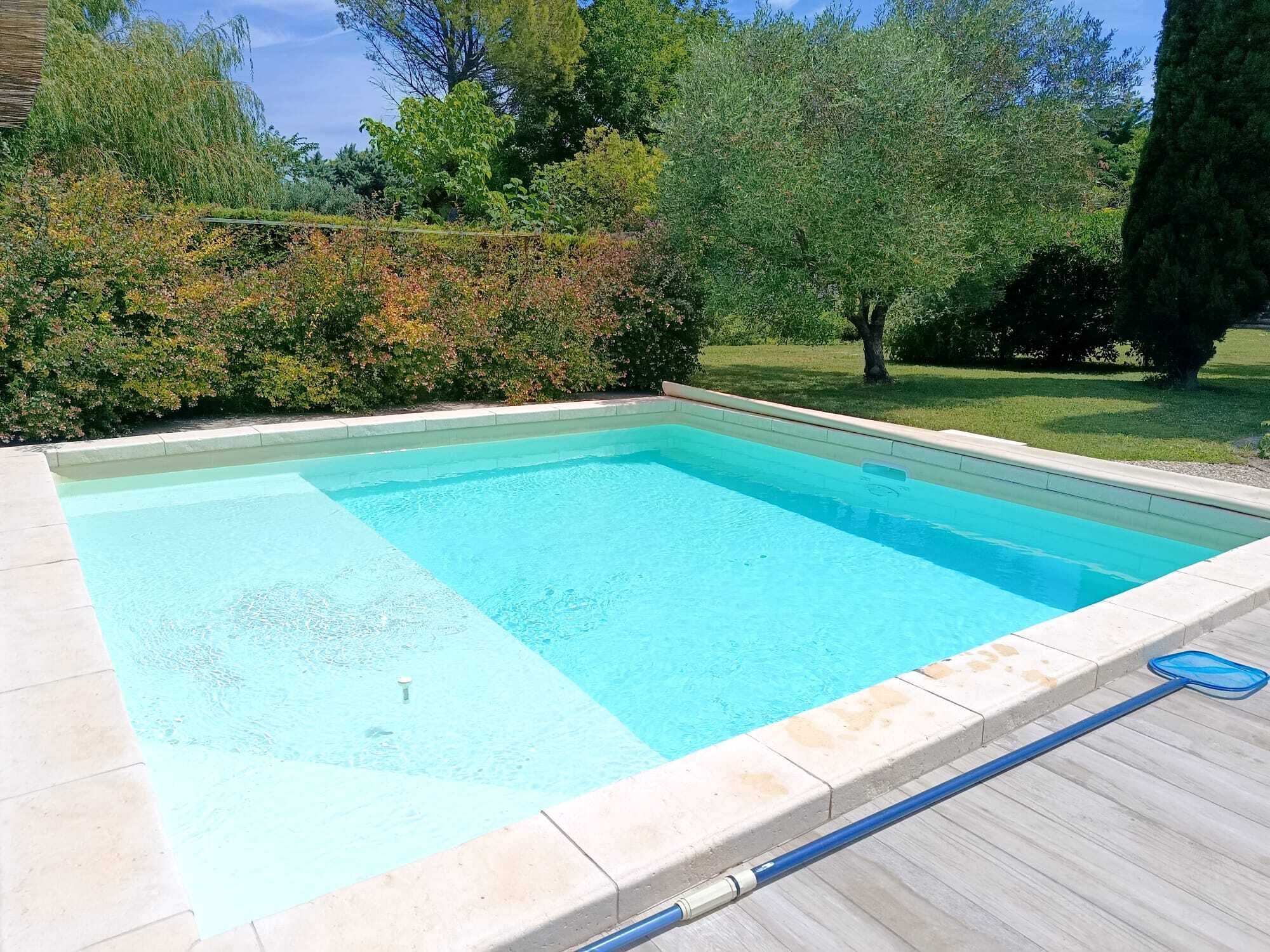 A rectangular swimming pool with a tiled edge, surrounded by a wooden deck and lush greenery.