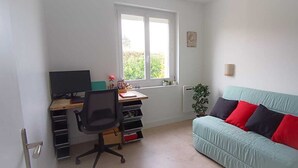Una habitación con escritorio, silla y sofá verde claro con cojines rojos y negros.
