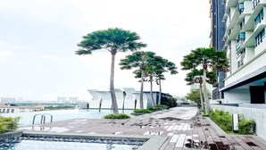 A modern hotel pool area with a wooden deck, palm trees, and a view of the city skyline. - Kajang MKH Boulevard Apartments (Kajang)