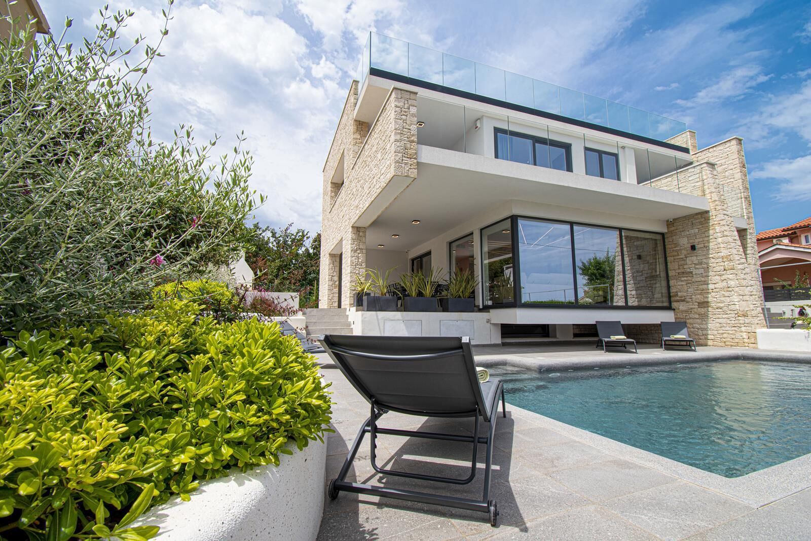 Une maison moderne dotée d’une piscine, d’un espace salon extérieur et d’une façade en pierre.