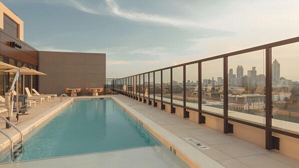 A rooftop pool with a city view, lounge chairs, and a modern building facade.