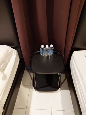 A hotel room with two beds, a small black table with water bottles, and a curtain. - Sea Lion Hotel Pulau Ketam (Pulau Ketam)