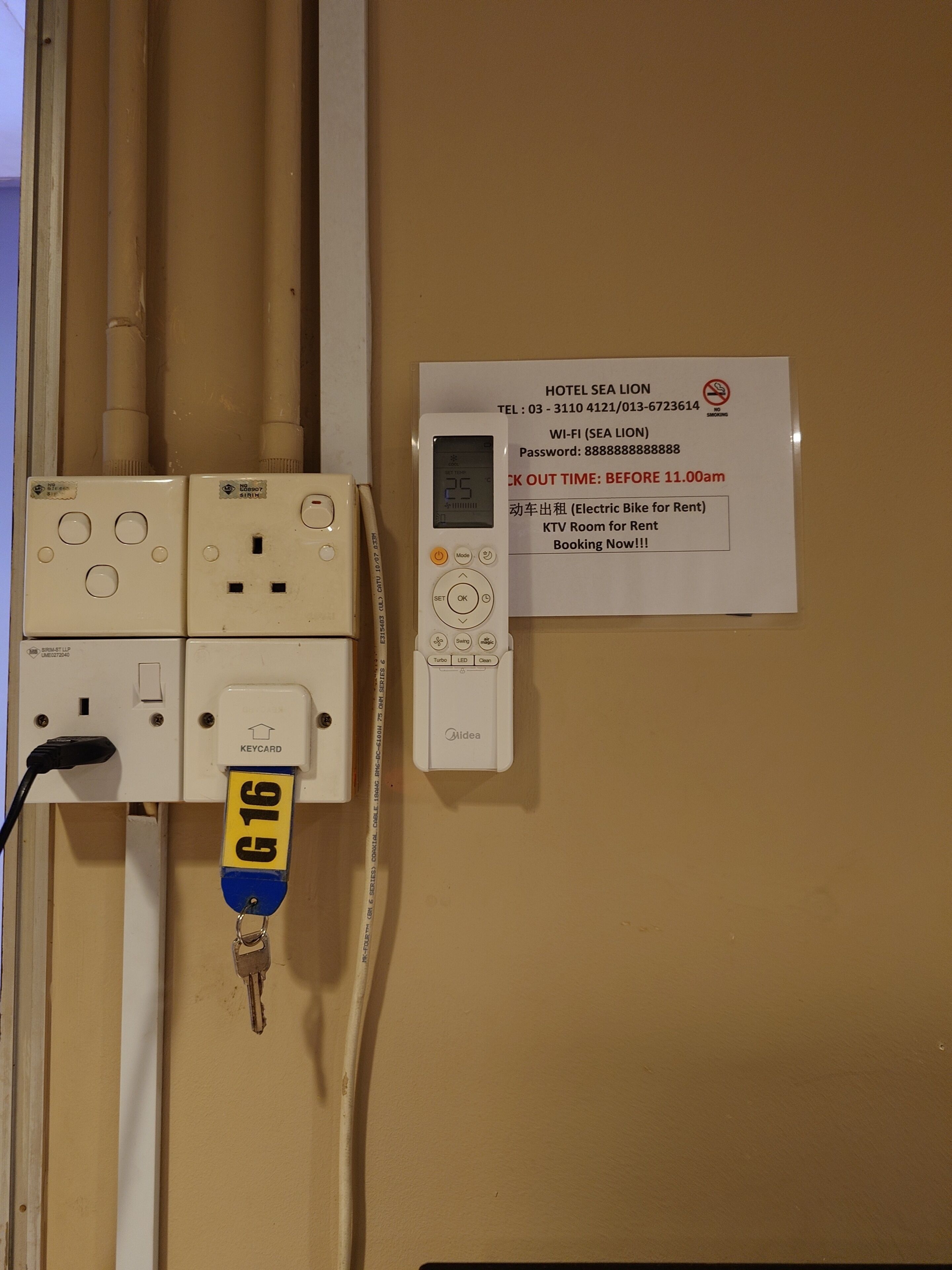 Painel elétrico fixado na parede, com leitor de cartão-chave, visor digital e placa com informações de contacto do hotel.