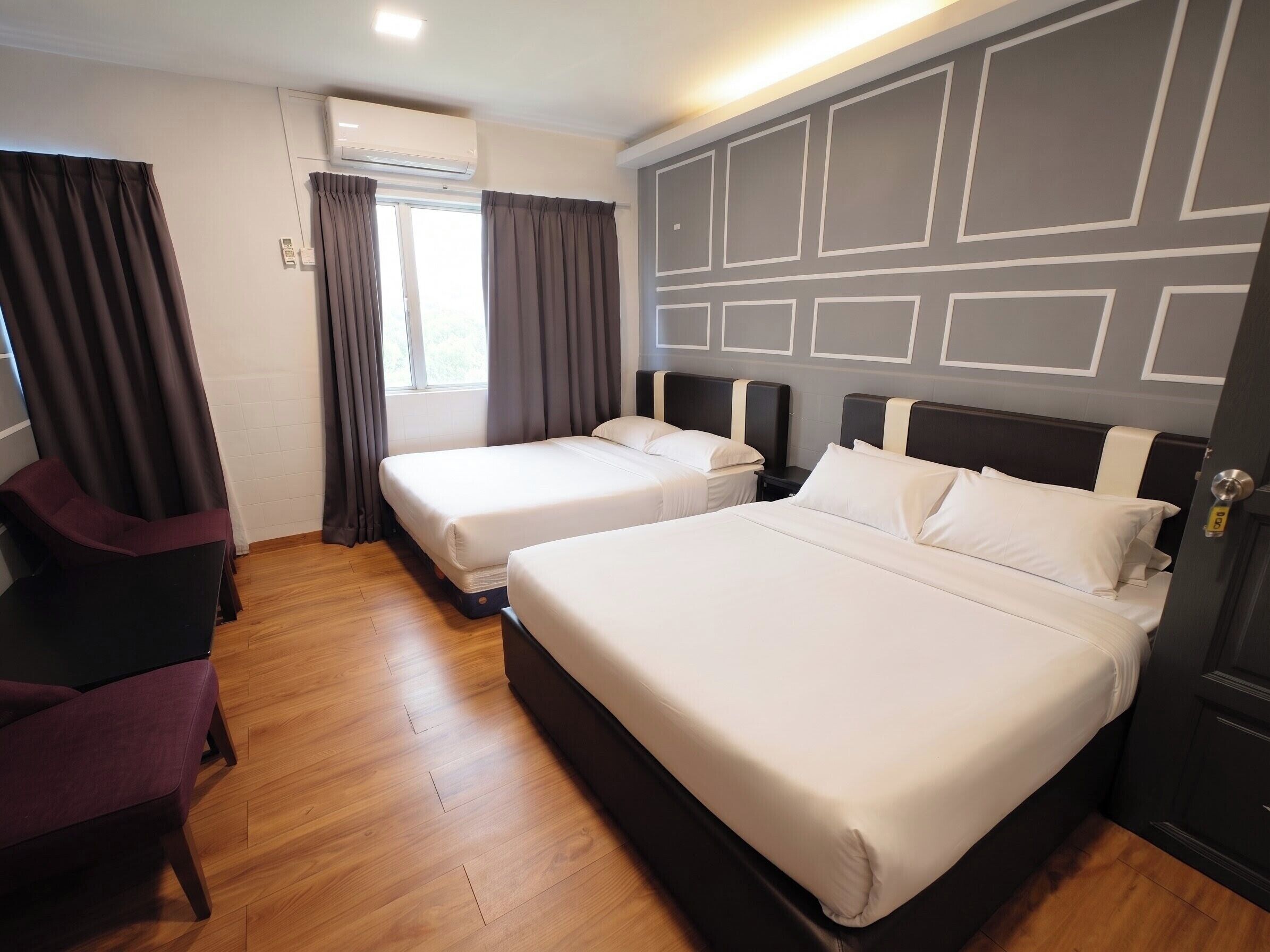 Een hotelkamer met twee bedden, een houten vloer, een raam met gordijnen en een airconditioner.