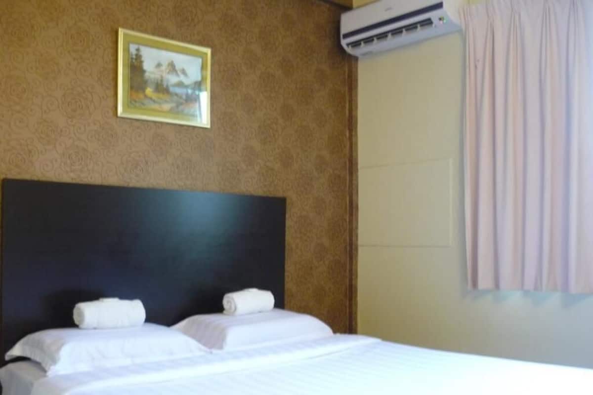 A hotel room with a bed, a painting on the wall, and an air conditioning unit.