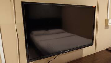 A flat-screen TV mounted on a wall, a wooden desk, and a white power outlet.