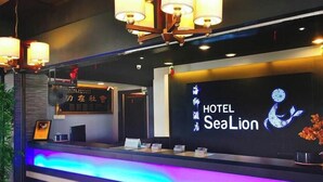A hotel reception desk with a neon sign for HOTEL SeaLion, a reception area with a plant, and a blue-lit counter.