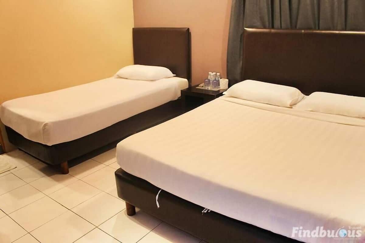 A hotel room with two single beds and one double bed, each with white linens. There is a small table with a tray of toiletries.