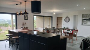 A modern kitchen with a central island, bar stools, pendant lights, and a dining area with a table and chairs. - New villa T4 Sotta between land and sea (Sotta)