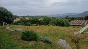 A rural landscape with a grassy field, scattered rocks, and a small building with a tiled roof. - New villa T4 Sotta between land and sea (Sotta)