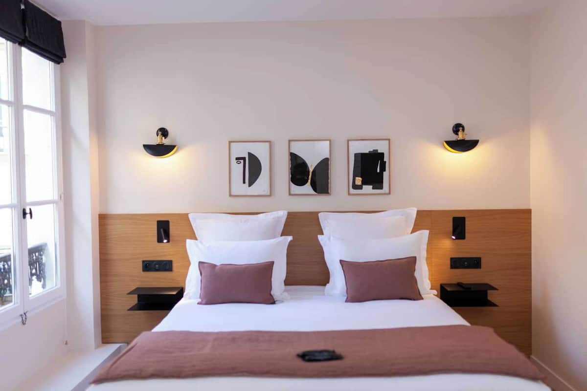 A hotel room with a large bed, two bedside tables, a nightstand, and a window with a view.