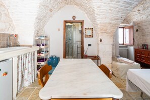 A rustic kitchen with a stone arch, a marble countertop, wooden chairs, a bed, and a radiator.
