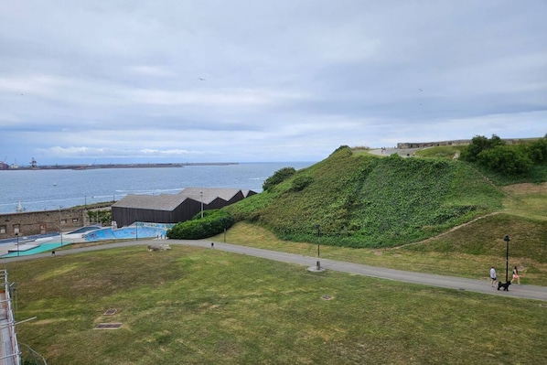A coastal landscape with a grassy area, a swimming pool, and a building with a sloped roof.