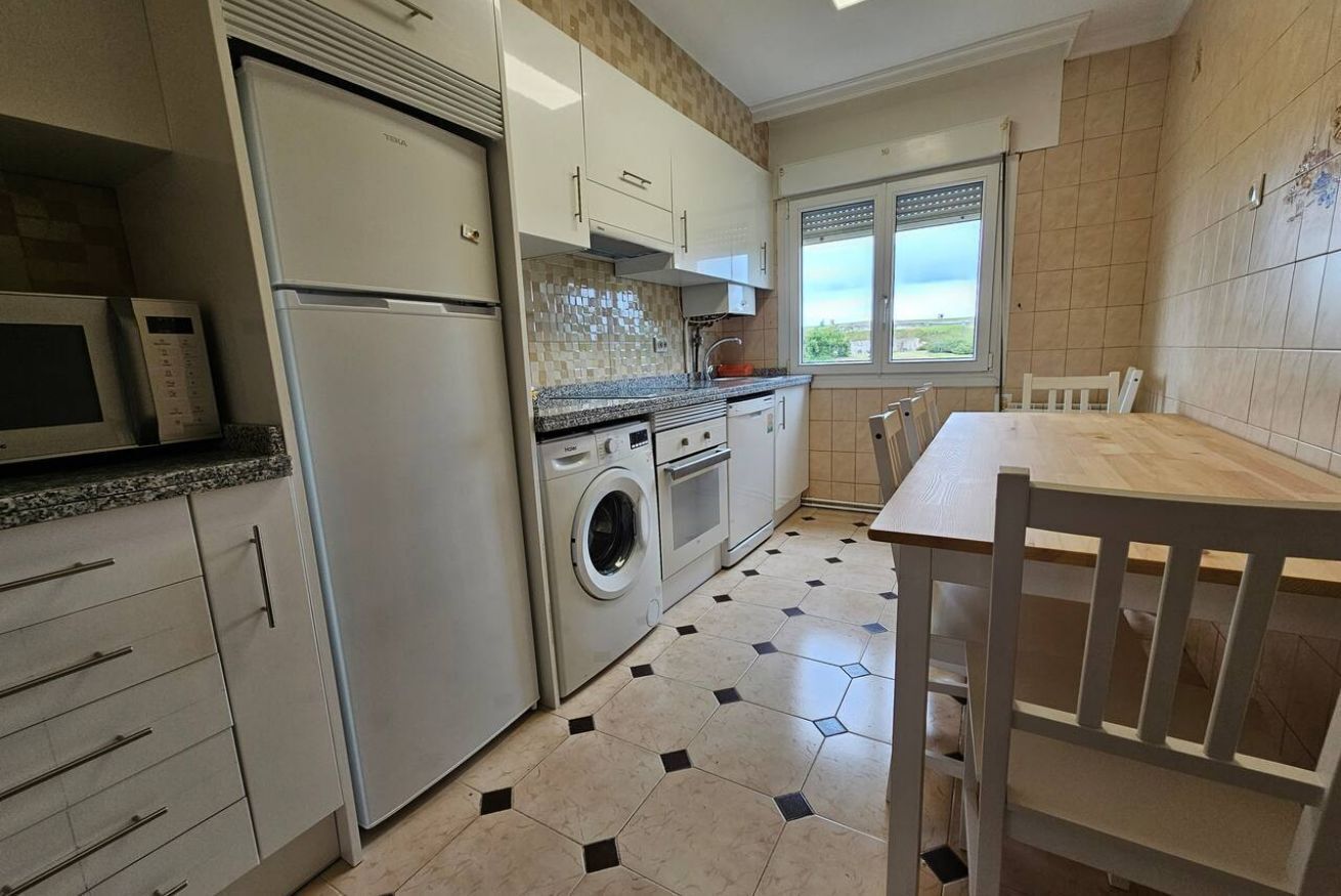 Een keuken met een wasmachine, magnetron en een eethoek met tafel en stoelen.