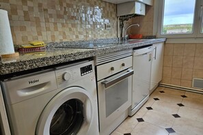 Una cocina compacta con lavadora Haier, horno empotrado y ventana con vistas.