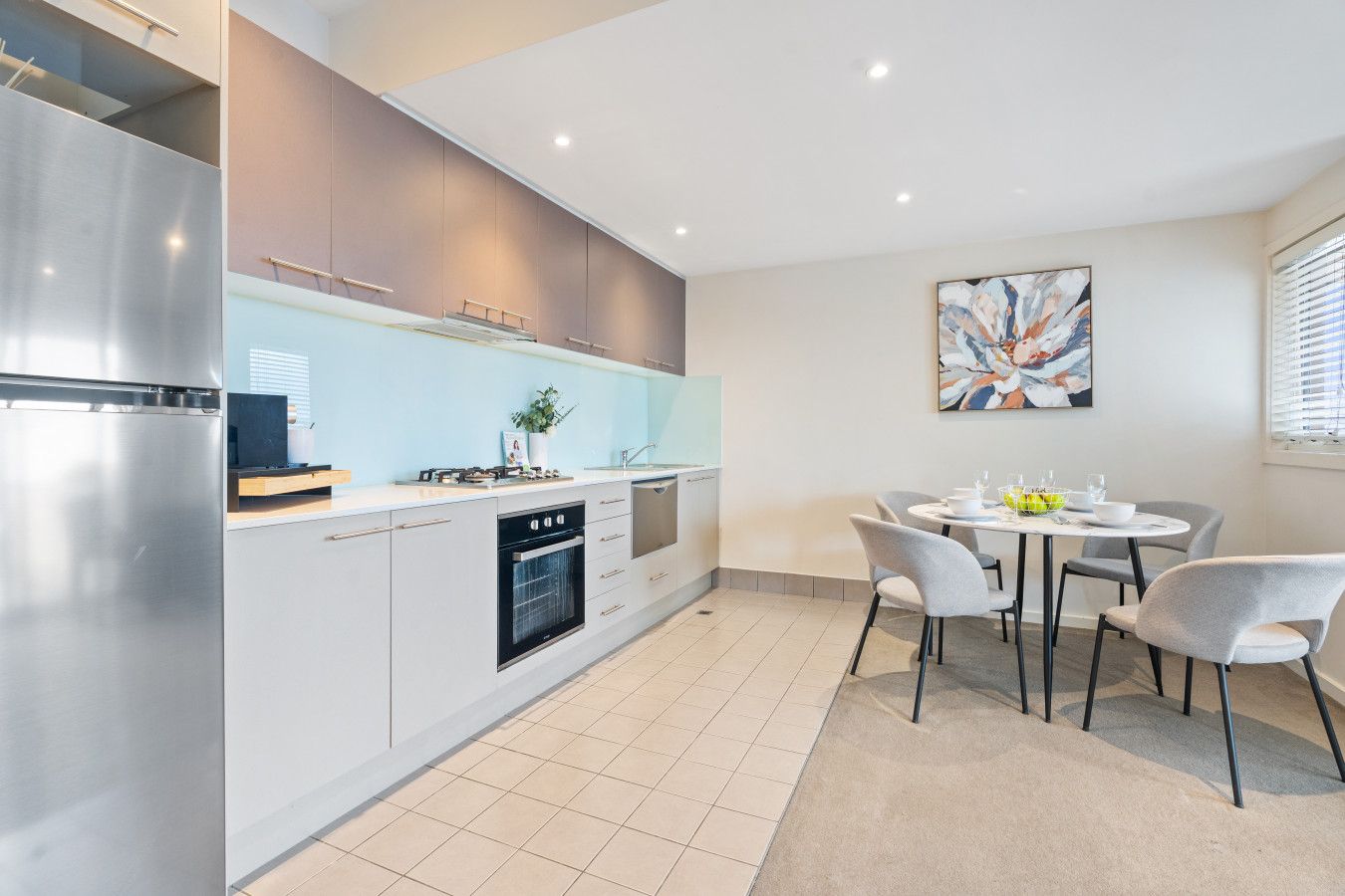 A modern kitchen with a stainless steel refrigerator, built-in oven, and a dining area with a round table and four chairs.