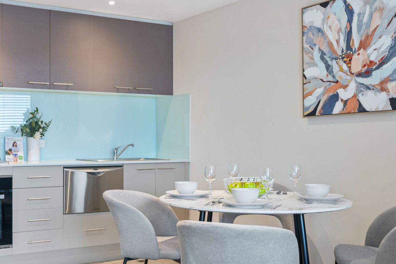 A modern kitchen with grey cabinets, a white countertop, and a dining area with grey chairs and a table set for four.