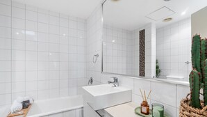 A modern bathroom with white tiles, a freestanding bathtub, a vanity with a sink, and a mirror.