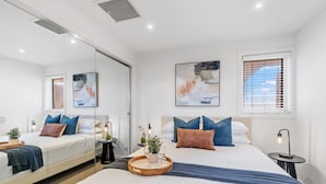 A modern hotel room with two beds, a large window with blinds, and artwork on the walls.